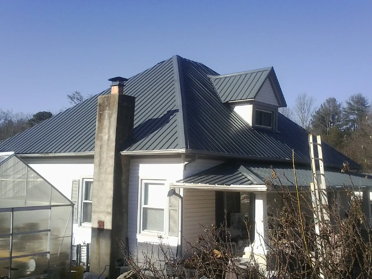 Dark blue standing seam metal roof on a white farmhouse with dormer — Slate & Tile Roof Repair by Roofing Brothers in Plainwell