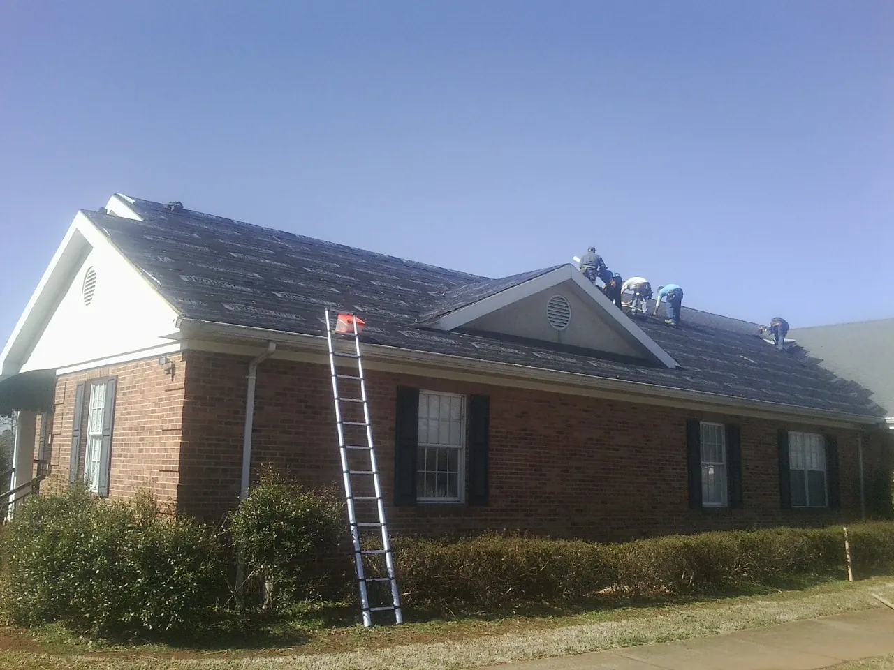 Crew tearing shingles off a brick ranch roof with a ladder set — Emergency Roof Repair work by our crew in Plainwell