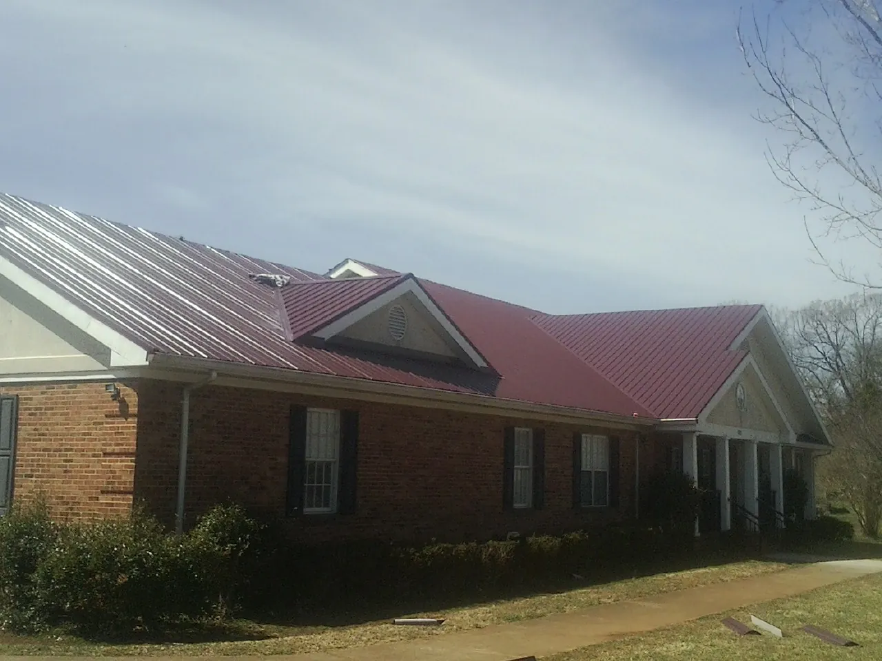 Red metal roof with gabled entries on a long brick building, from a Hail Damage Roof Repair job in Plainwell