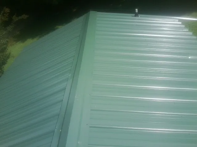 New green metal panels meeting at the ridge of a roof — Flat Roof Repair work by our crew in Plainwell