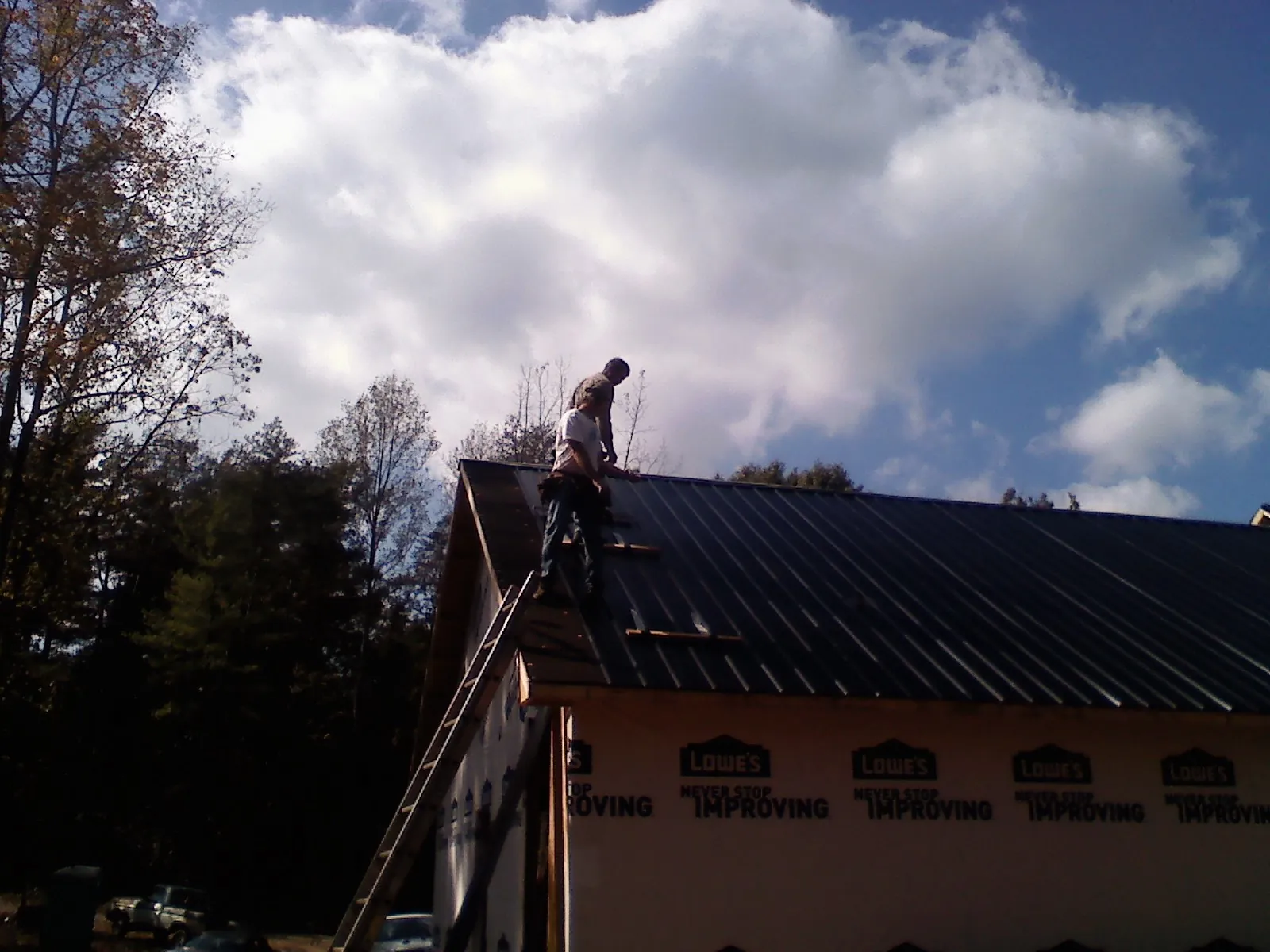 Roofer fastening dark metal panels high against a cloudy sky, from a Roof Inspection job in Plainwell